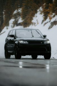 A modern black SUV travels on a snowy mountain road, showcasing winter travel. Un SUV noir moderne voyageant sur une route de montagne enneigée, mettant en valeur les voyages hivernaux.