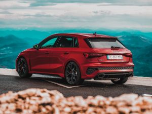 A stunning red sportback car parked with a scenic mountain backdrop, showcasing luxury automotive design. Une magnifique voiture sportback rouge garée avec un décor de montagne pittoresque en arrière-plan, mettant en évidence un design automobile de luxe.