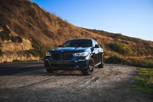 Blue BMW X6 M parked on a scenic road in Newport Beach, CA at sunset. Un BMW X6 M bleu garé sur une route pittoresque à Newport Beach, en Californie au coucher du soleil.