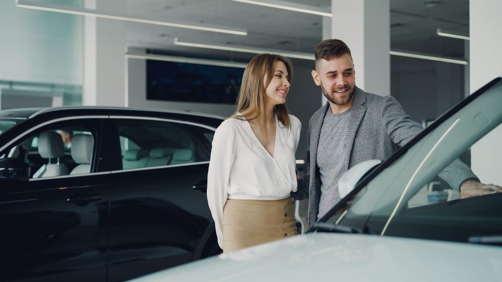 Smiling couple exploring cars at dealership, enjoying shopping experience. Couple souriant explorant les voitures chez un concessionnaire, appréciant l'expérience d'achat.
