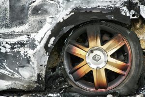 Gros plan détaillé d'une roue de voiture brûlée avec jante rouillée et pneu endommagé, montrant les conséquences du feu.