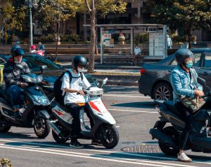 People riding scooters in a busy urban street with helmets and masks in Taipei. Des gens font du scooter dans une rue urbaine animée avec des casques et des masques à Taipei.