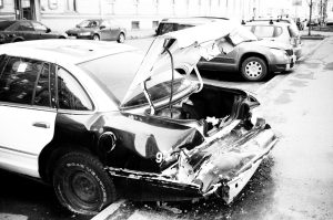 A black and white photo of a wrecked car on an urban street, highlighting vehicle damage. Une photo en noir et blanc d'une voiture épave dans une rue urbaine, mettant en évidence les dégâts du véhicule.