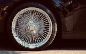 Detailed view of a classic spoked wheel rim on a black car, showcasing retro style. Vue détaillée d'une jante à rayons classique sur une voiture noire, mettant en avant un style rétro.